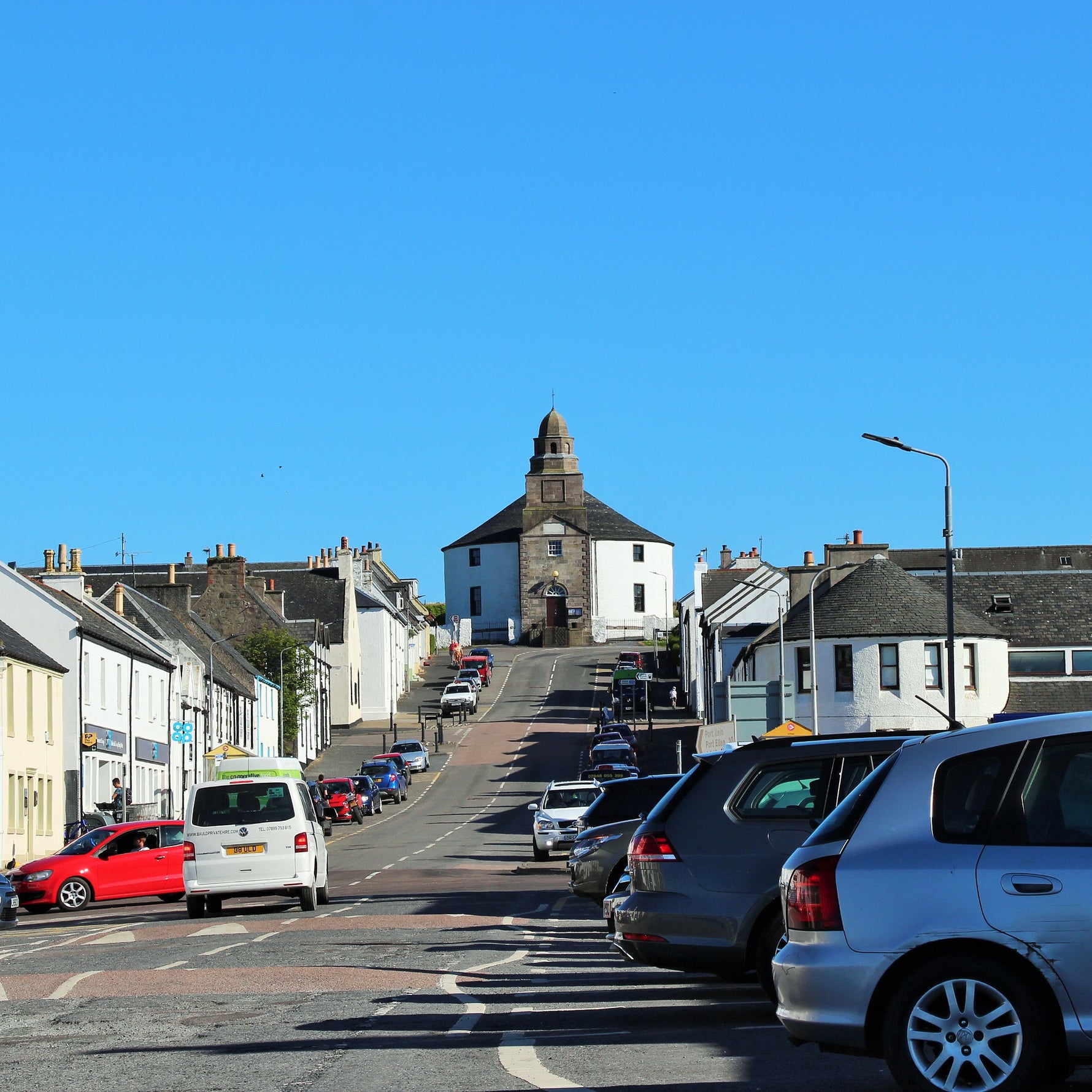 Bowmore village main street on the Isle of Islay Scotland on a sunny day – home of Bowmore Distillery Est. 1779, the oldest distillery on Islay, with the iconic round church at the top of the hill | 蘇格蘭艾雷島波摩村主街 波摩蒸餾廠所在地 1779年創立 圓形教堂